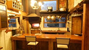 A rustic kitchen with wooden cabinets, a large stove, and hanging pots. - Hostel Punta Ballena Bar (Punta Ballena)