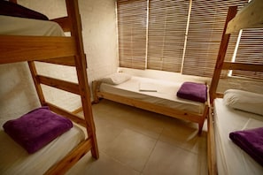 A dormitory room with bunk beds, a window with blinds, and a bed with a purple towel. - Hostel Punta Ballena Bar (Punta Ballena)