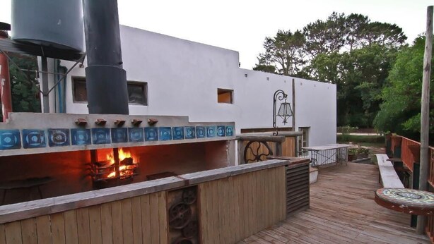 A wooden deck with a barbecue area, a white building with a bell, and a water tank. - Hostel Punta Ballena Bar (Punta Ballena)