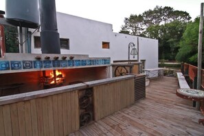 A wooden deck with a barbecue area, a white building with a bell, and a water tank. - Hostel Punta Ballena Bar (Punta Ballena)