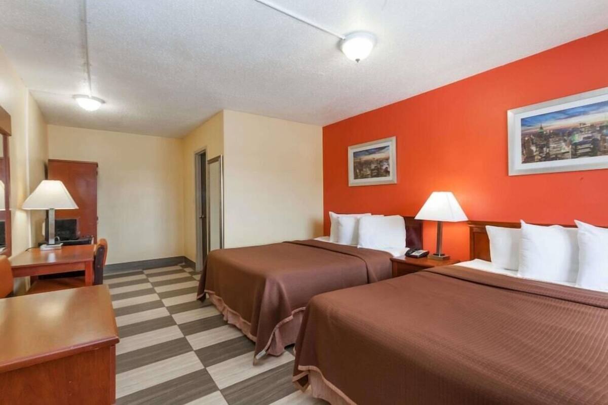A hotel room with two beds, a desk, a chair, and a check-in counter.