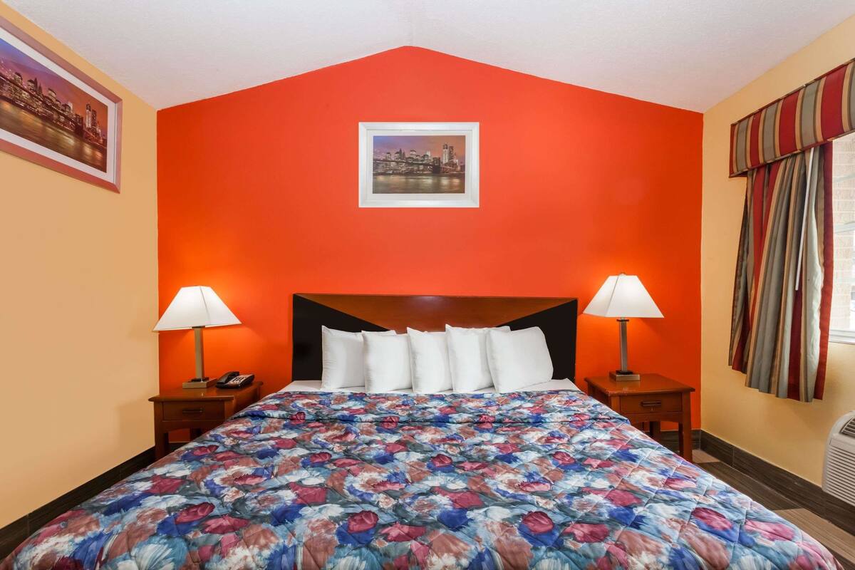 A hotel room with a large bed, two bedside tables with lamps, a framed picture on the wall, and a window with curtains.