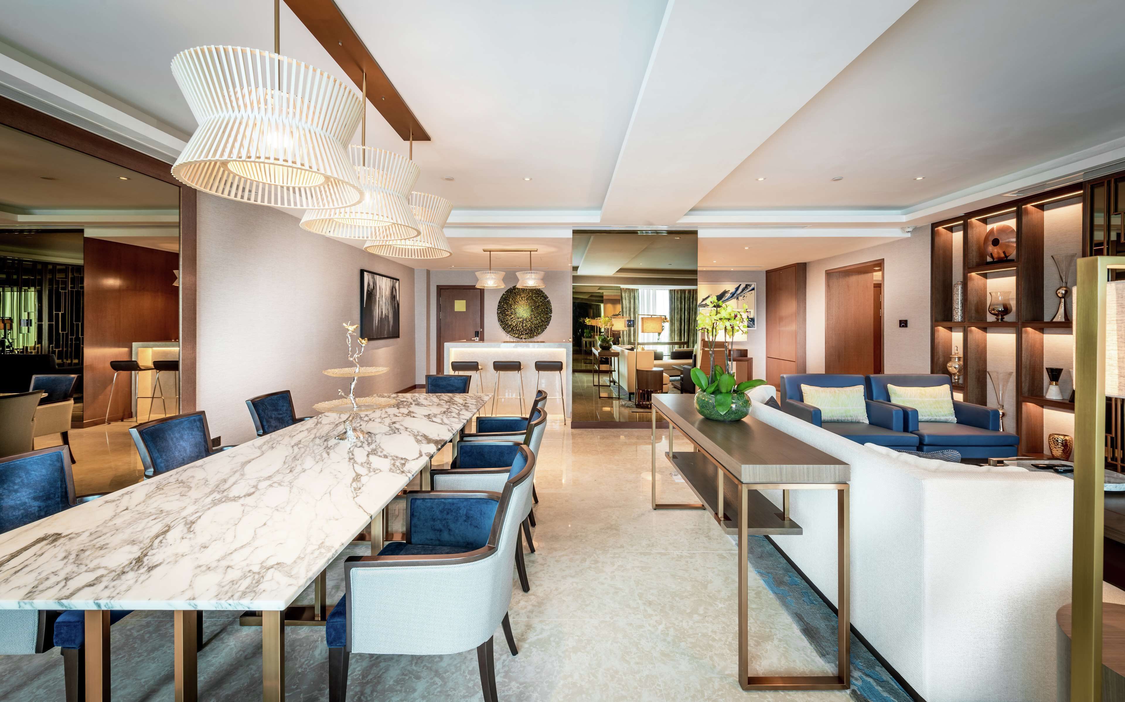 A modern hotel lobby with a marble reception desk, a bar area, and a seating area with sofas and a coffee table.