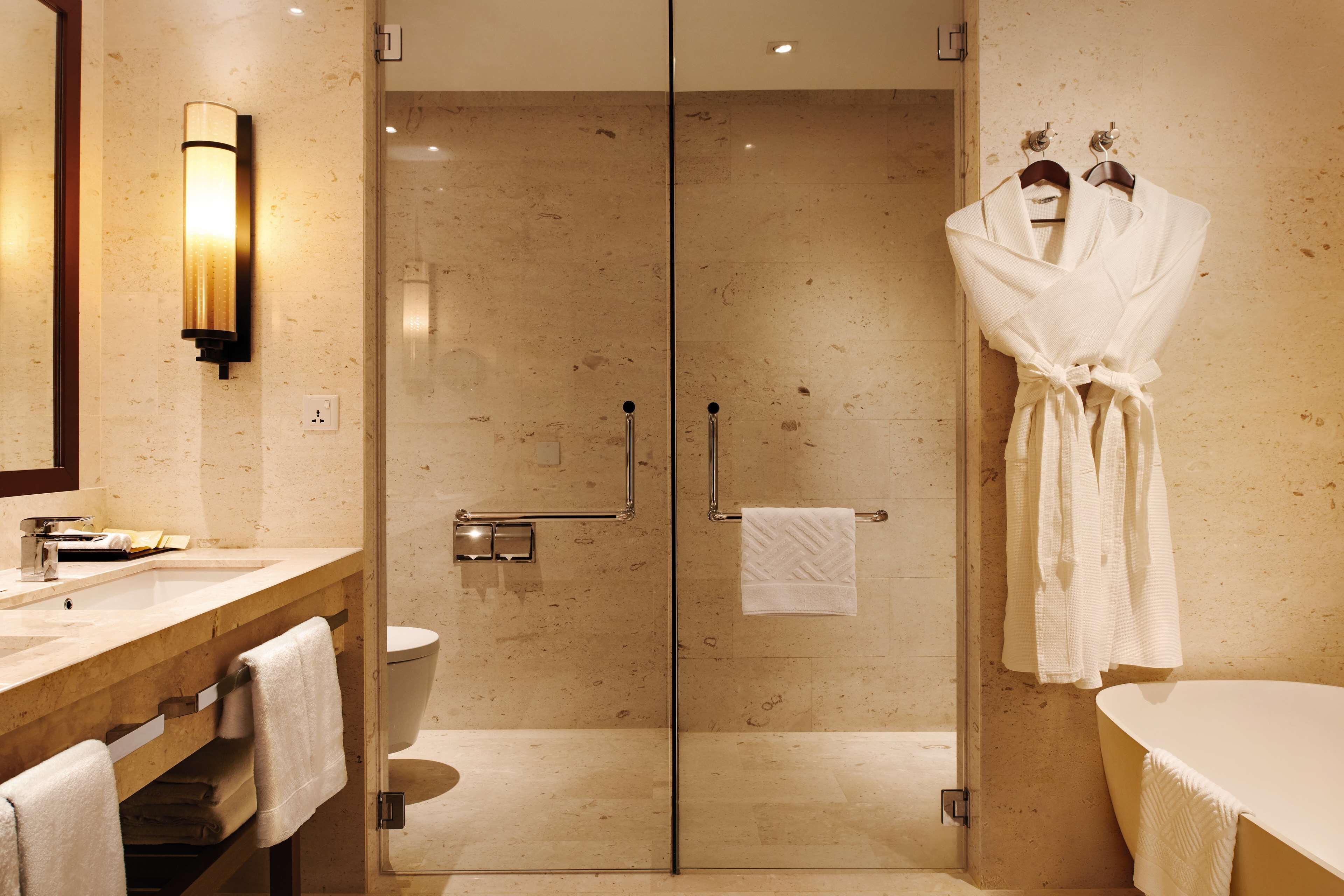 Une salle de bain moderne avec une douche à parois de verre, un meuble-lavabo en bois doté d’un porte-serviettes et une baignoire blanche.