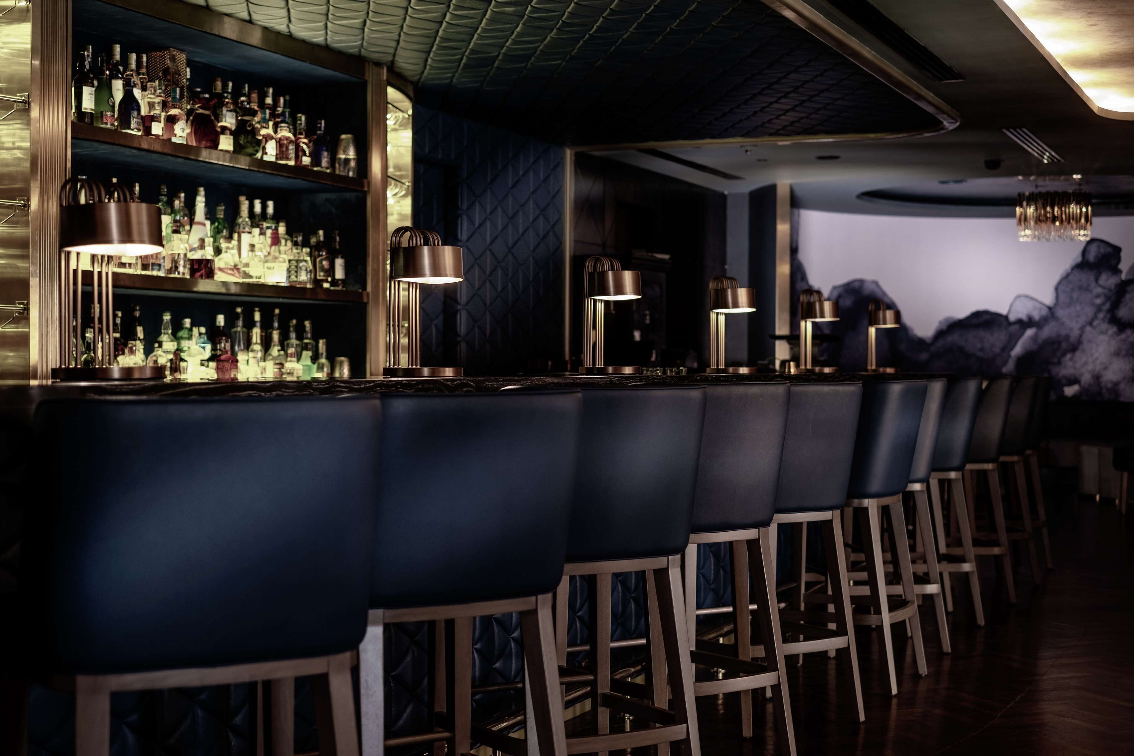 A bar area with multiple shelves of bottles, bar stools, and pendant lighting.