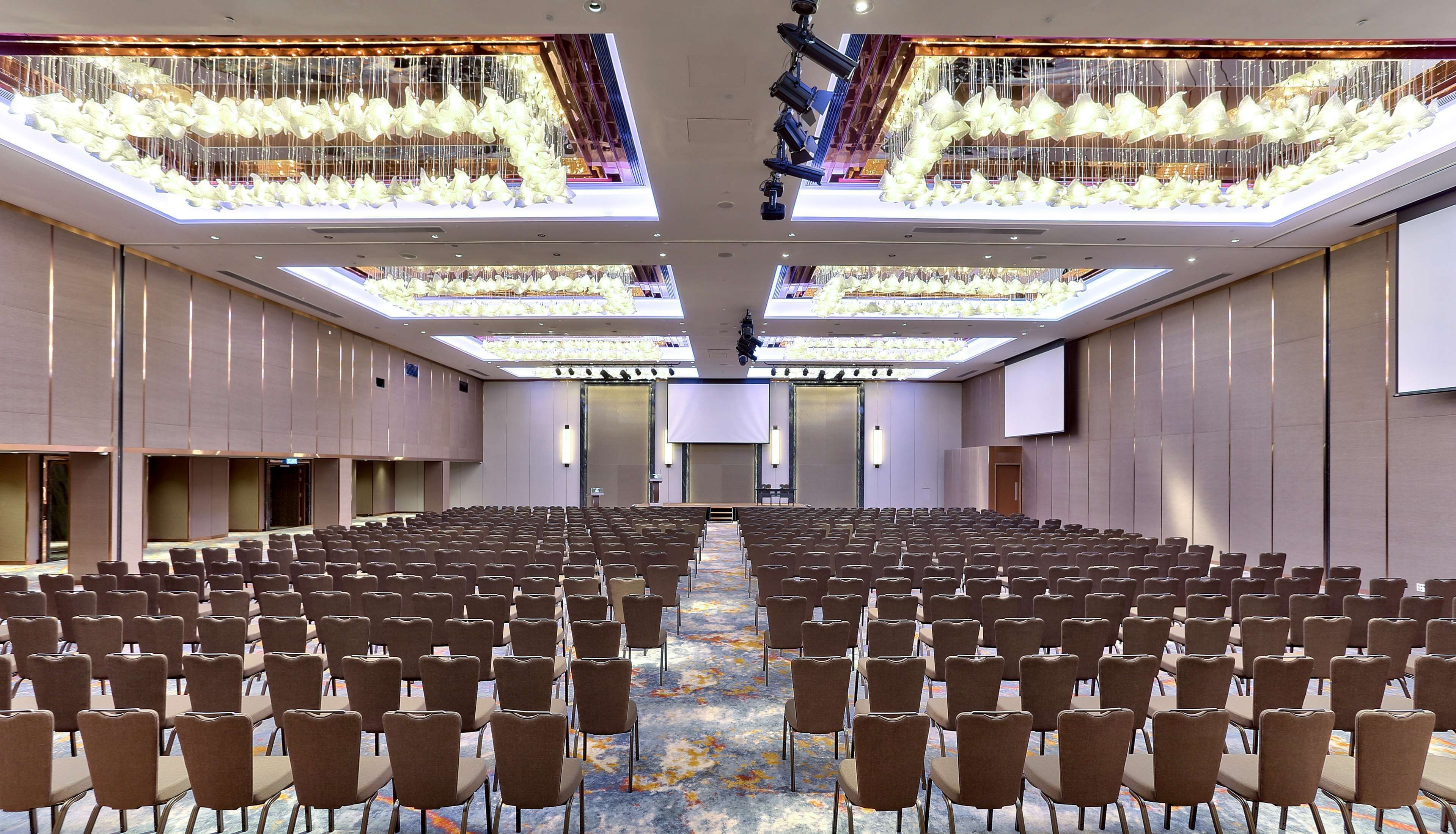 A large conference room with rows of chairs, a central stage, and a ceiling with hanging lights.