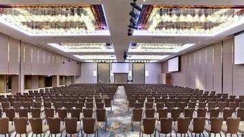 A large conference room with rows of chairs, a central stage, and a ceiling with hanging lights.