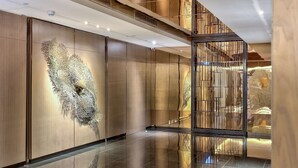 A modern lobby with a reflective floor, a large abstract wall art, and a view of a staircase. - Hilton Kota Kinabalu (Kota Kinabalu)