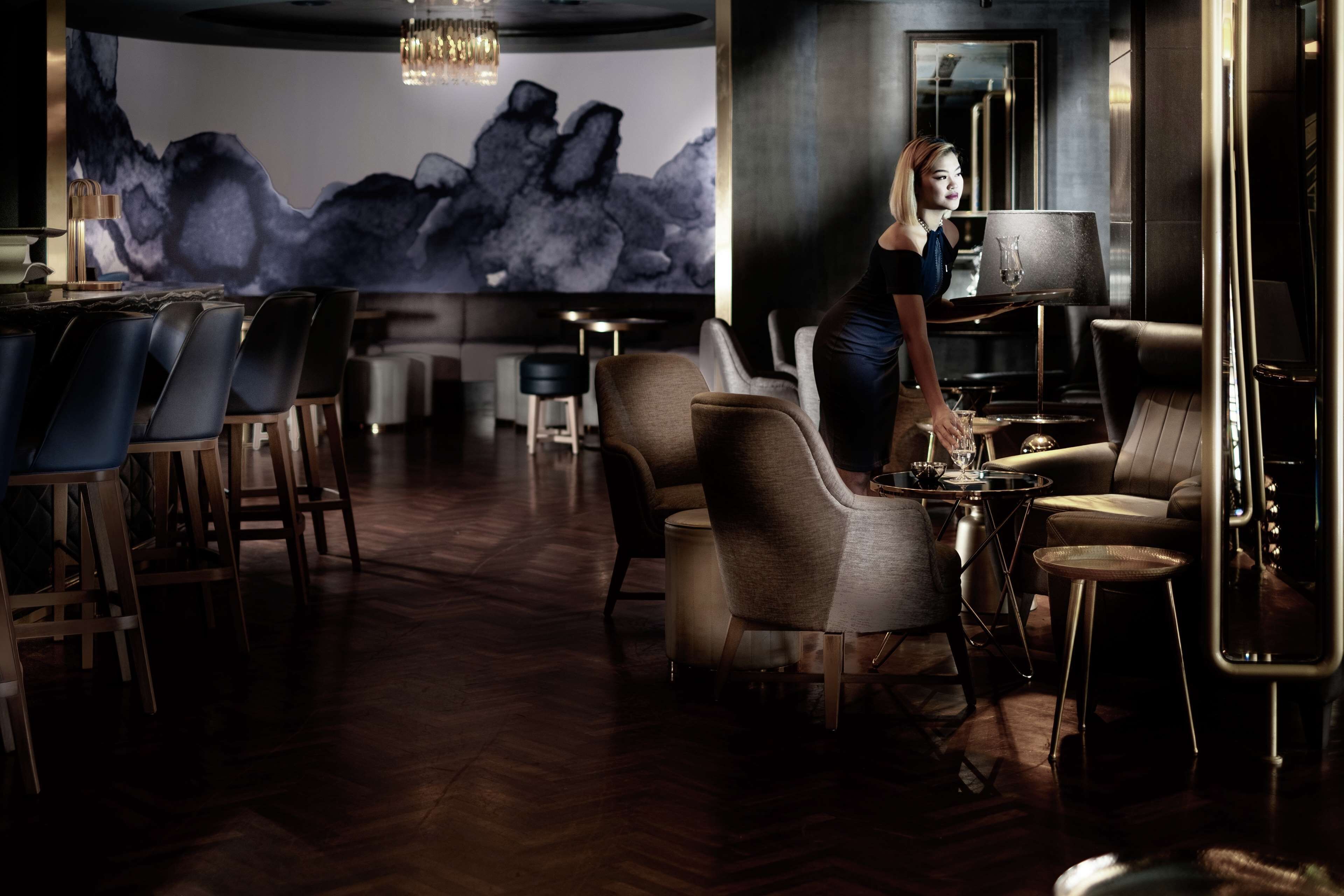 A modern bar area with a large abstract mural, comfortable seating, and a well-lit ambiance.