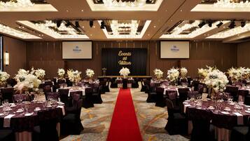 A banquet hall with round tables, red carpet, and floral centerpieces.