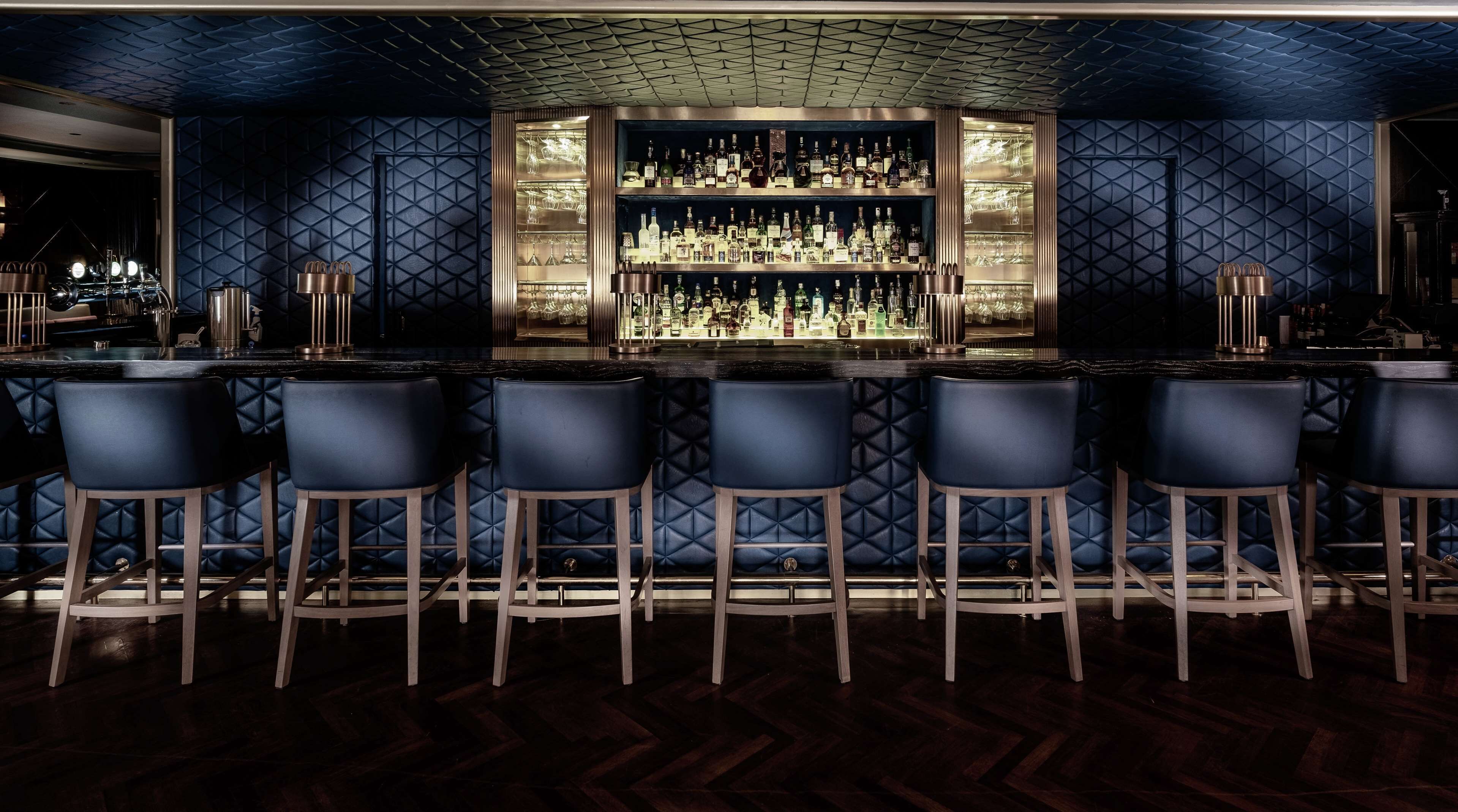 Un espace bar doté d’un plancher en bois foncé, d’un comptoir central et de six tabourets de bar.