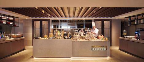 Un área de cocina moderna y bien iluminada, con un chef preparando comida, que cuenta con una isla central con diversos alimentos y un diseño elegante y contemporáneo.