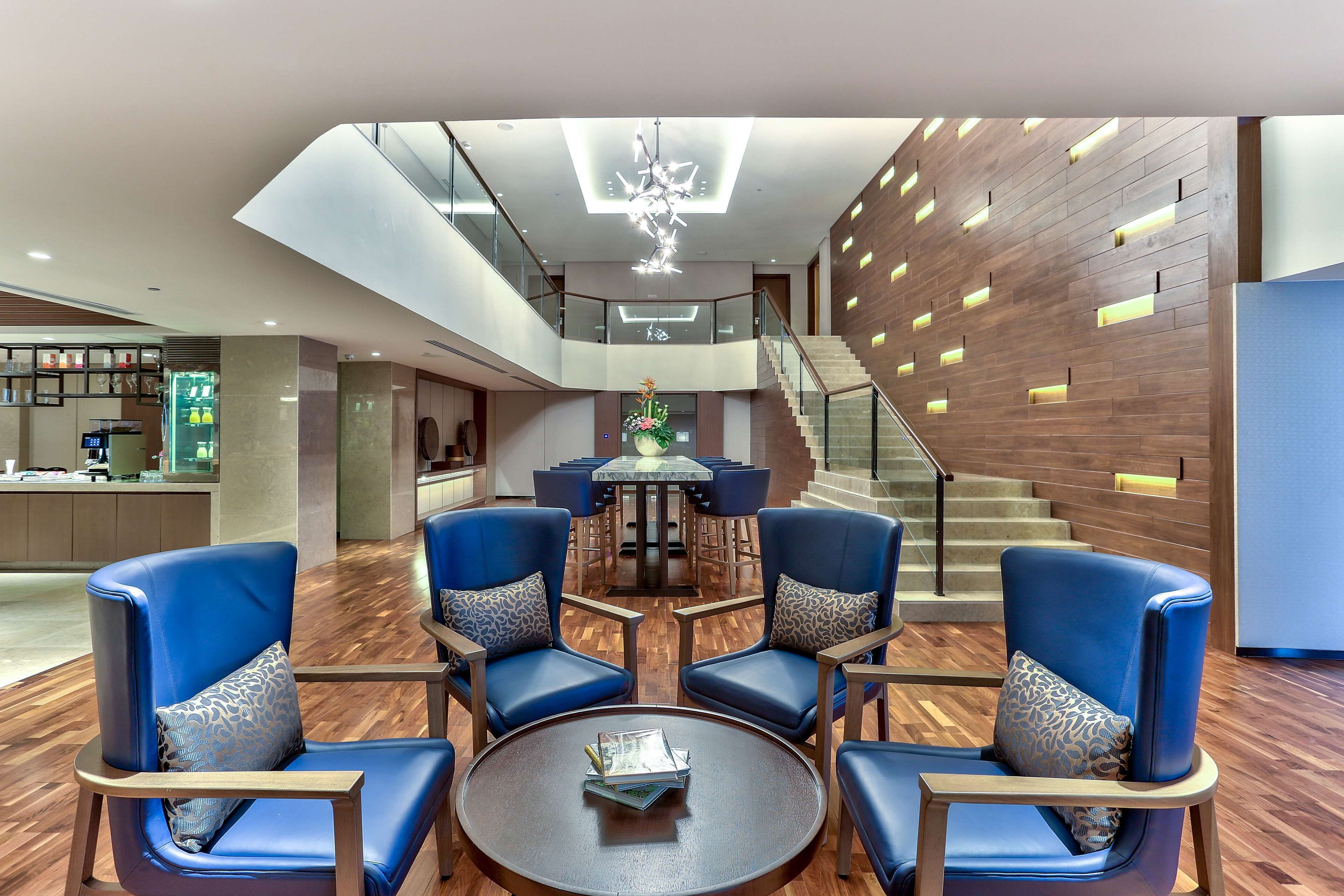 A modern lobby with a central seating area, a staircase, and a reception desk.