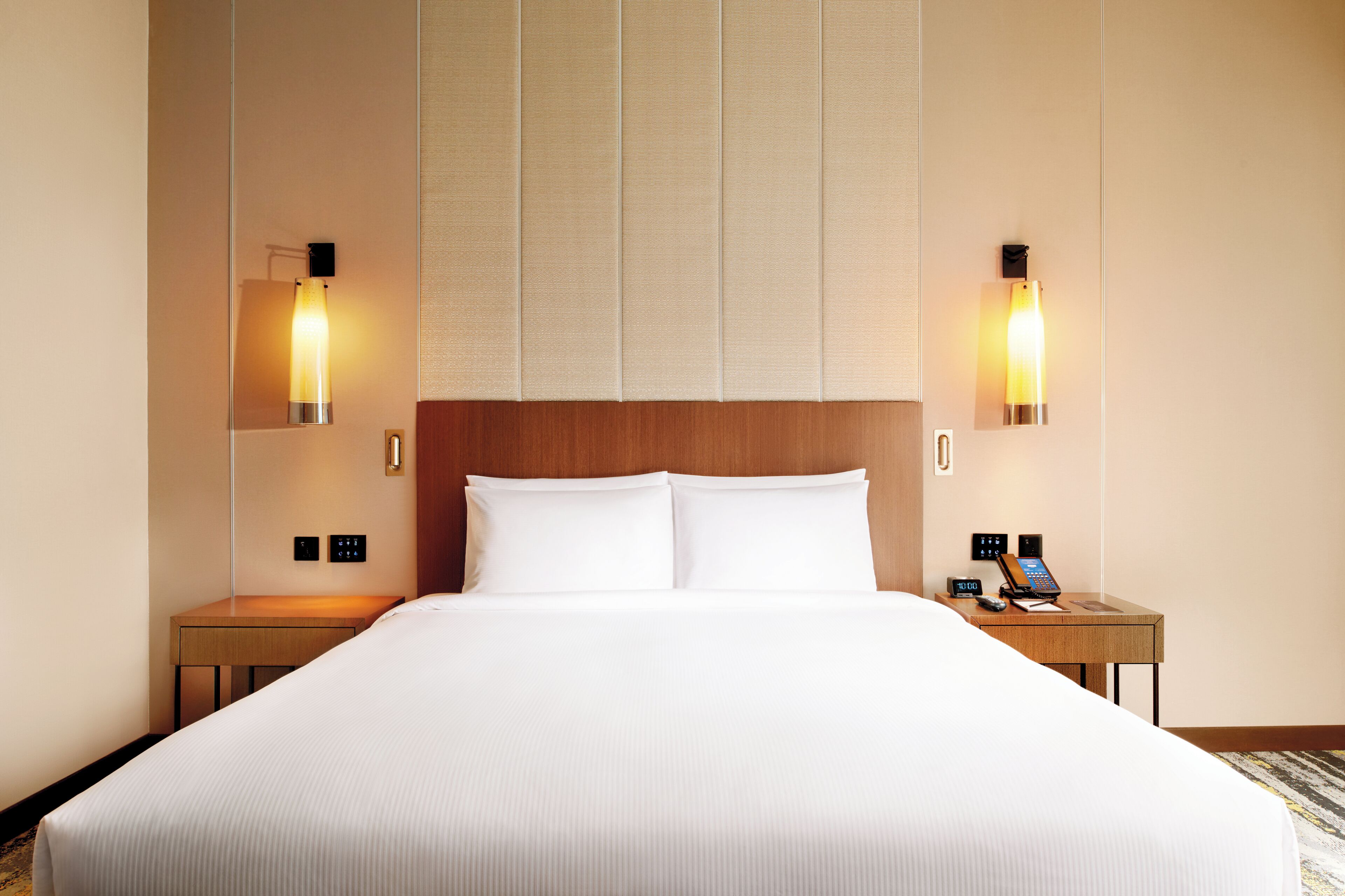 A hotel room with a large bed, two bedside tables, a wooden headboard, and wall-mounted lamps.