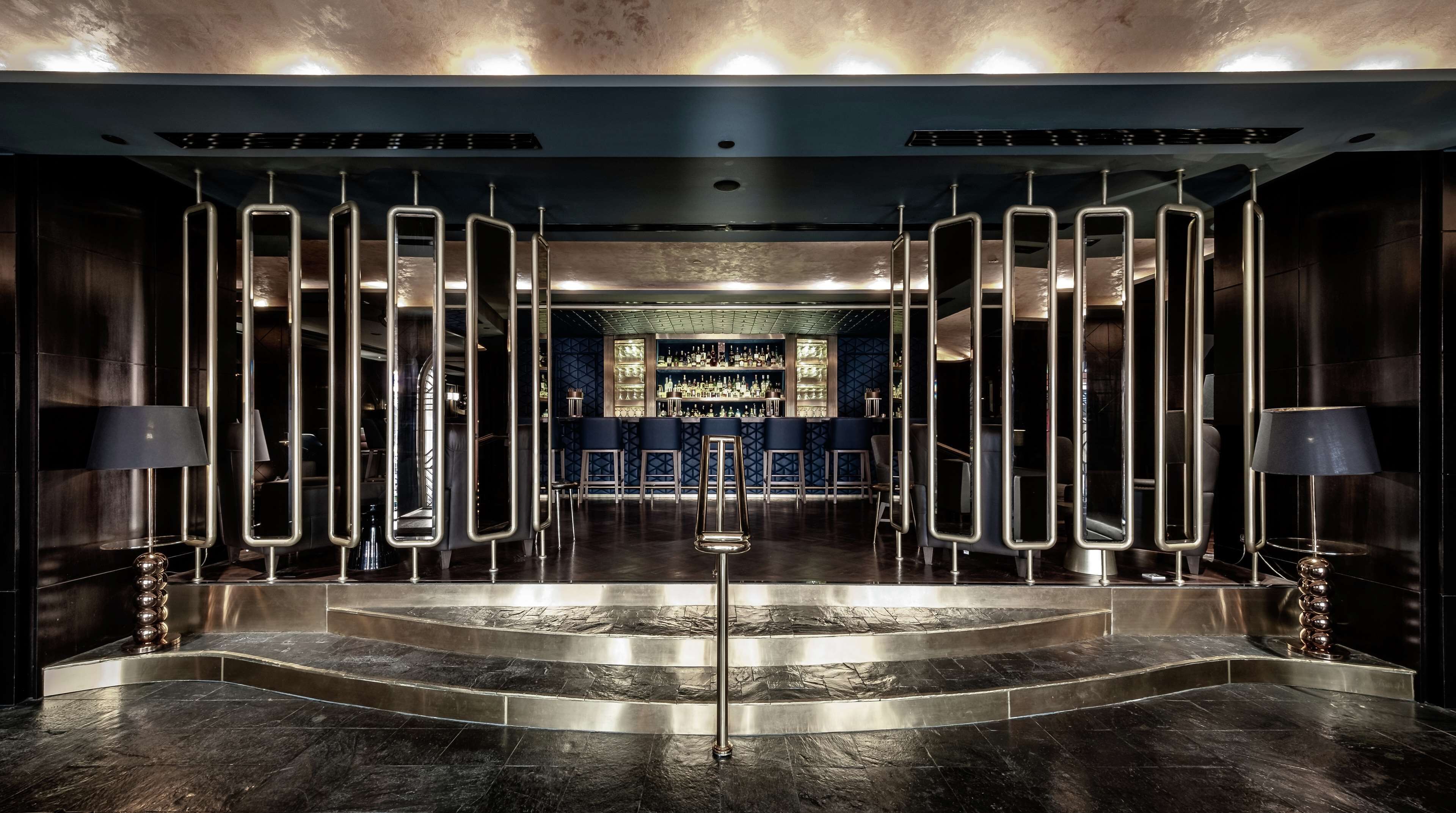 A modern bar area with a central staircase, mirrored partitions, and a bar stocked with bottles.