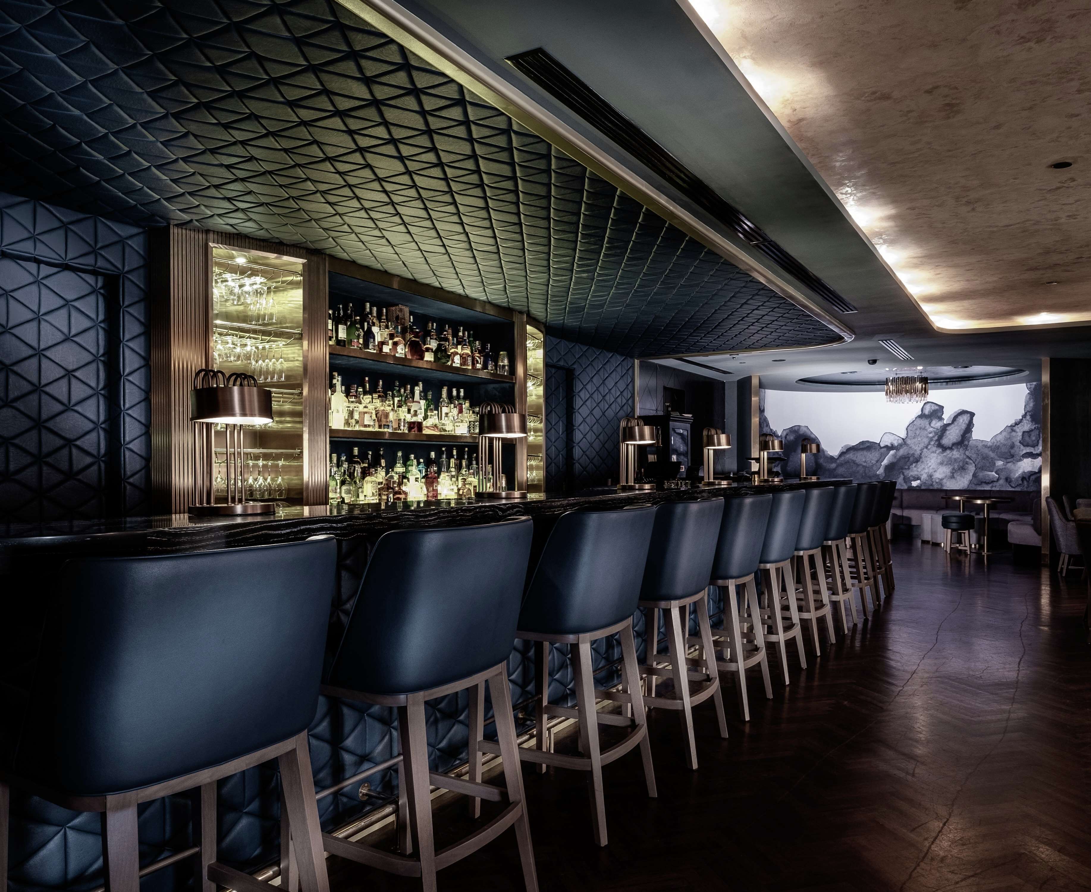 A bar area with a long counter, multiple stools, and a wall of liquor bottles.