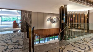 A modern hotel lobby with a marble floor, a wooden bench, a glass railing, and a decorative wall piece. - Hilton Kota Kinabalu (Kota Kinabalu)