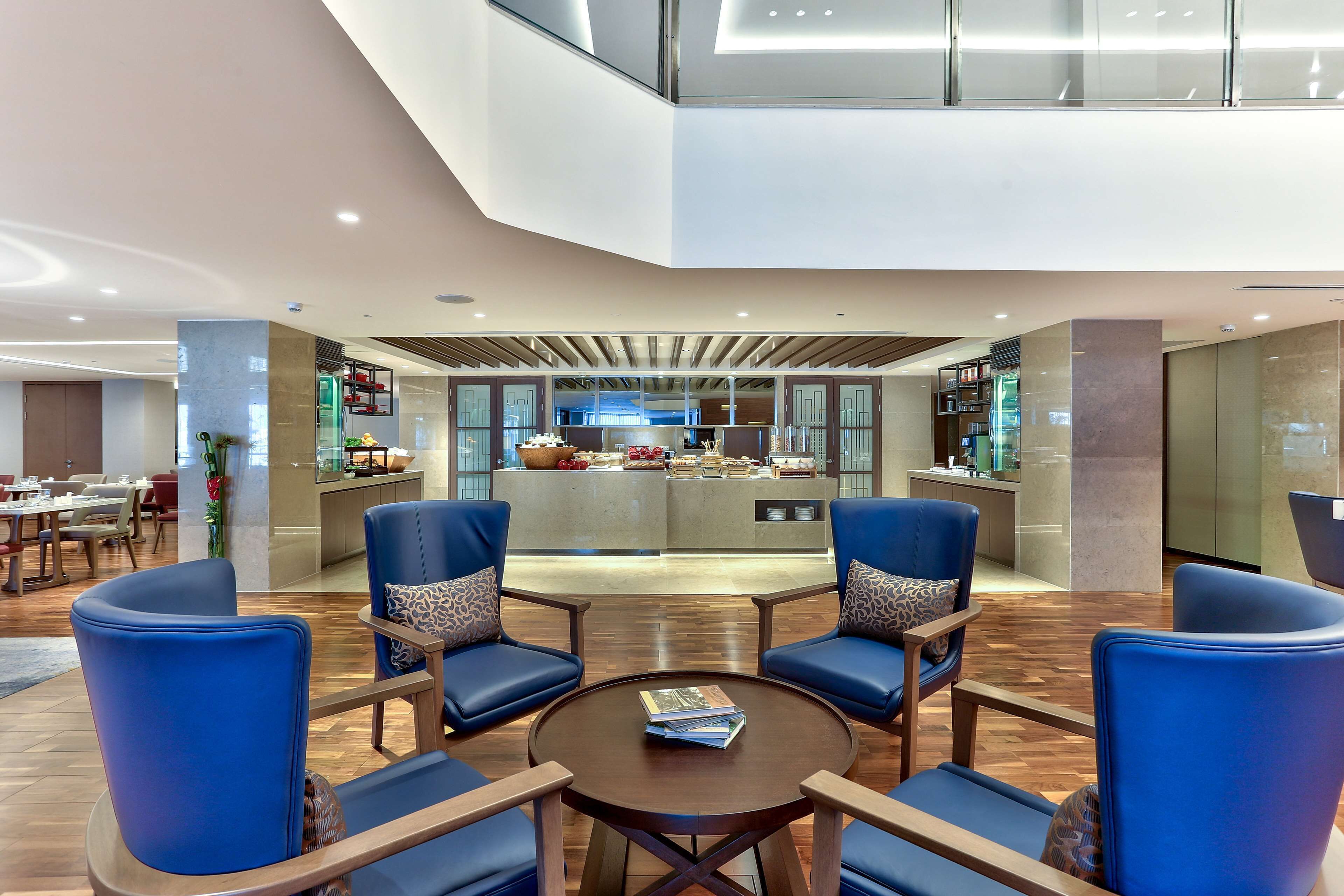 A modern hotel lobby with a central island, seating area, and a view of the kitchen.