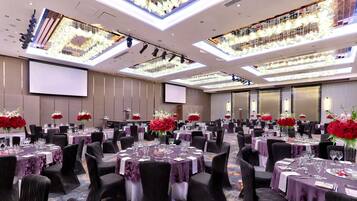 Un salón de banquetes con varias mesas redondas, cada una dispuesta con sillas, copas de vino y centros de mesa con flores rojas.