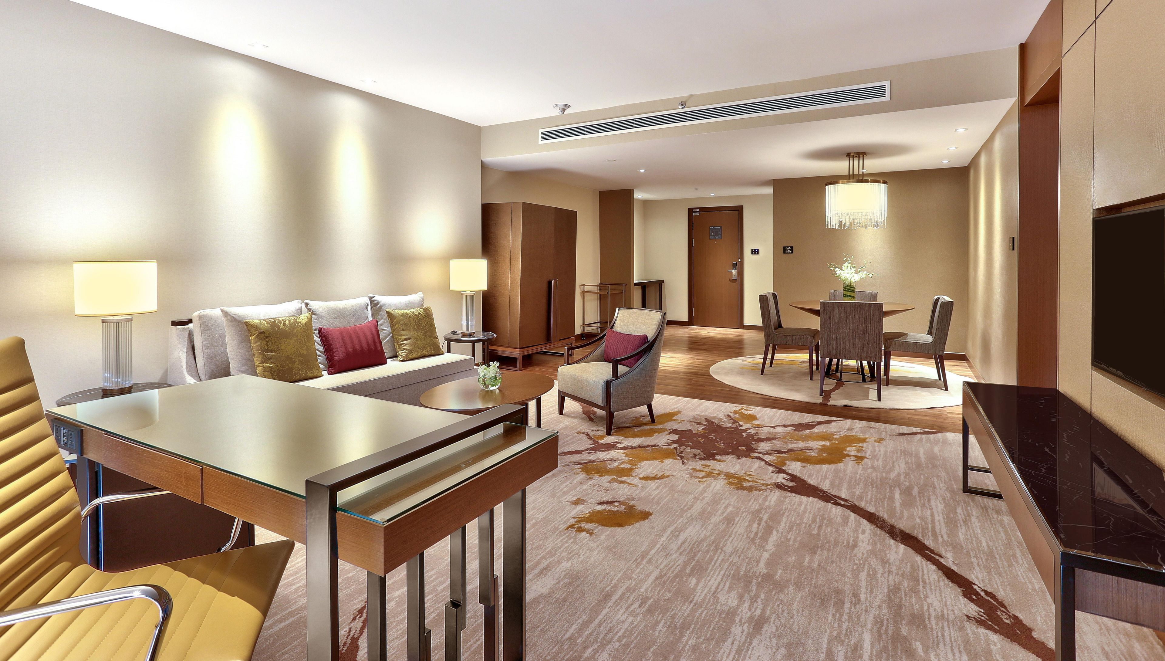 Habitación de hotel con sofá, mesa de comedor con sillas, televisor y lámpara.