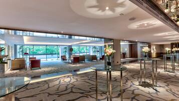 A spacious lobby with a patterned carpet, glass tables, and red chairs.