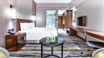 A hotel room with a bed, bedside table, lamp, TV, and a small table with a vase.