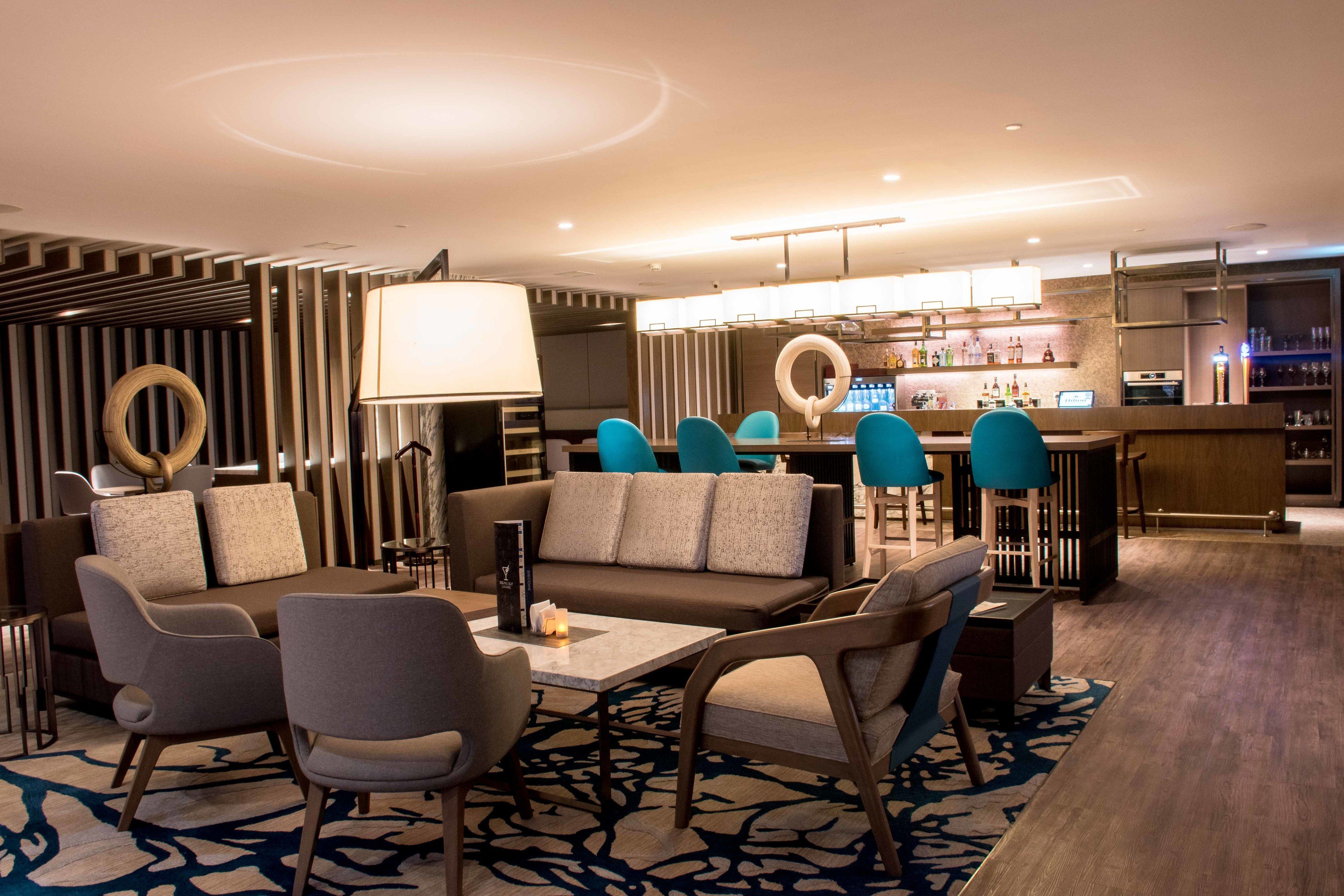 Un moderno vestíbulo de hotel con zona de bar, diferentes espacios de asiento y una cocina a la vista.