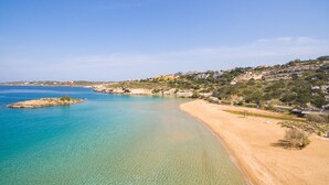 Eine Küstenlandschaft mit klarem Wasser, Sandstrand und Häusern am Hang.