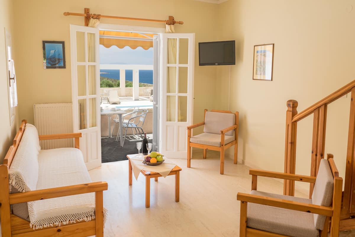 Una sala de estar acogedora con un sofá, sillones, una mesa de centro con fruta y vistas al mar a través de un ventanal abierto.