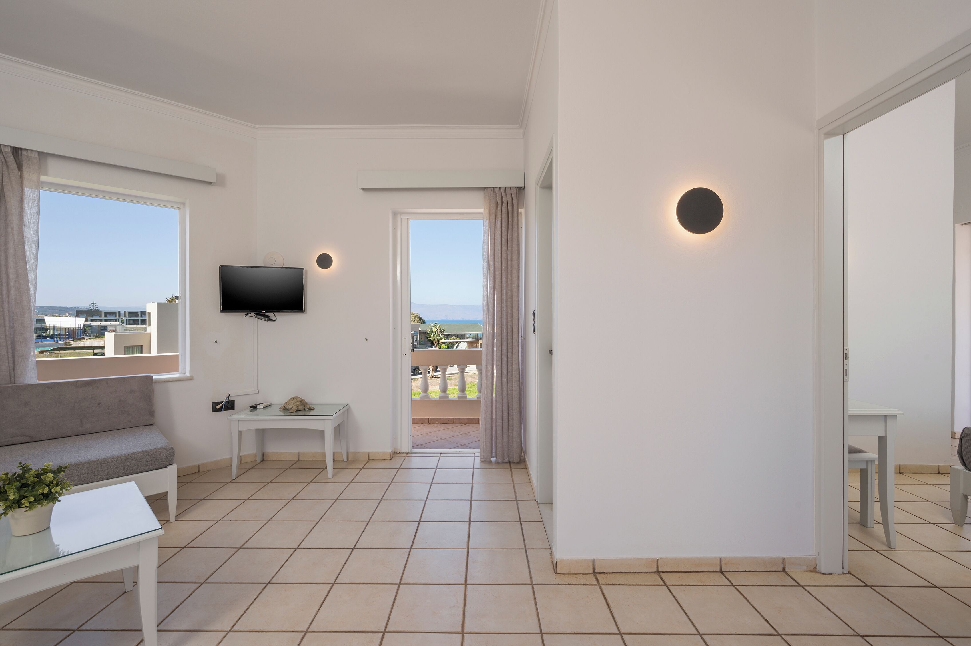 Una sala de estar moderna con televisor de pantalla plana, un sofá, una mesita y un balcón con vistas al mar.