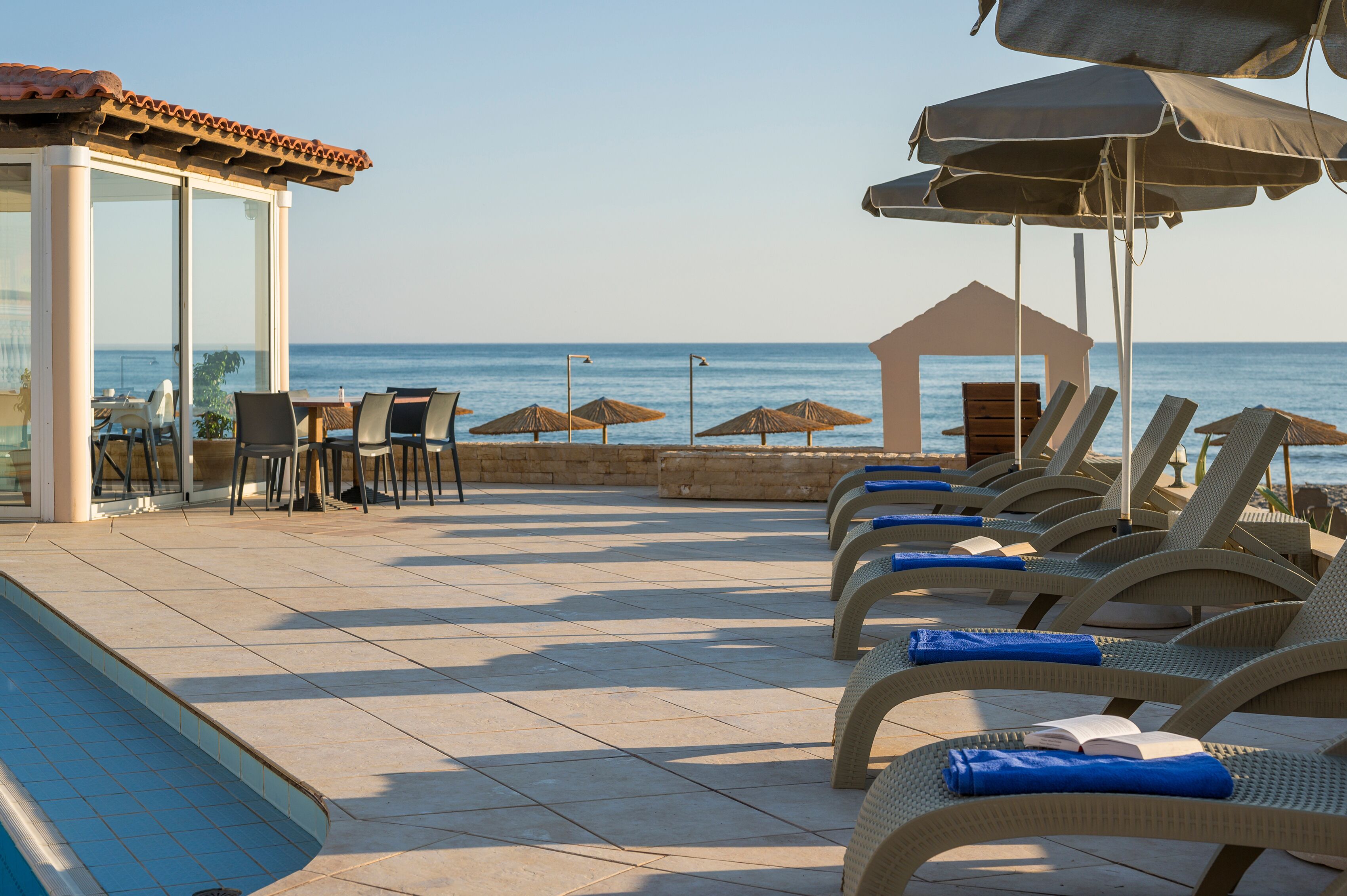 A poolside area with lounge chairs, umbrellas, and a glass-enclosed structure with tables and chairs.