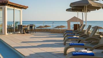 A poolside area with lounge chairs, umbrellas, and a glass-enclosed structure with tables and chairs.