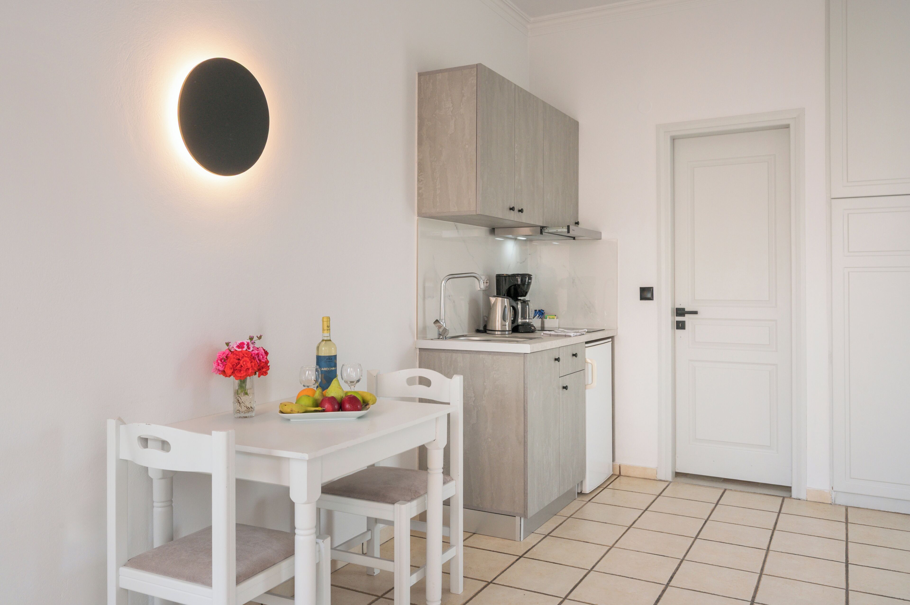 A compact kitchen with a white table, chairs, a coffee machine, and a cabinet.
