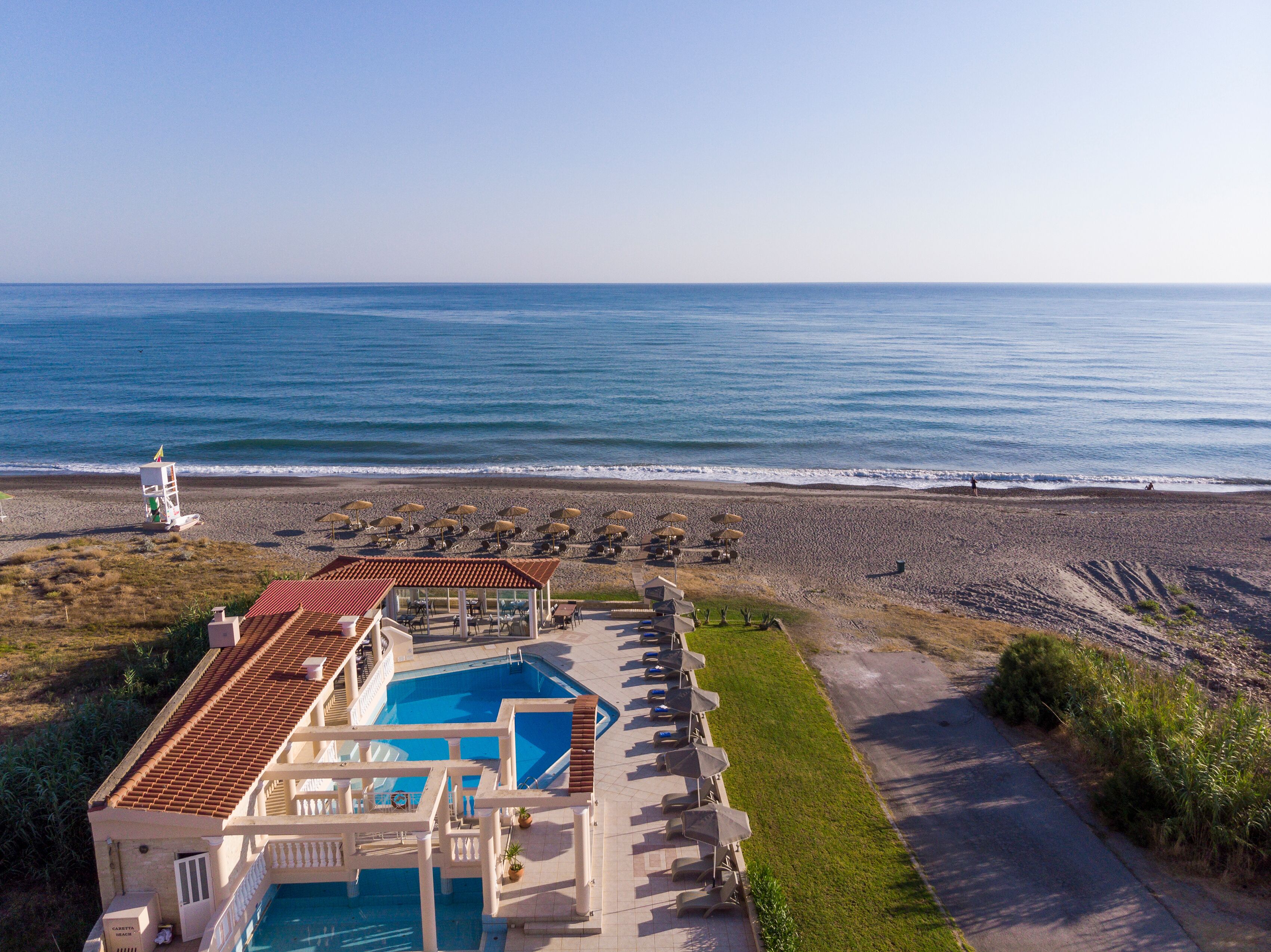 A resort with a swimming pool, beach umbrellas, and a lifeguard tower.