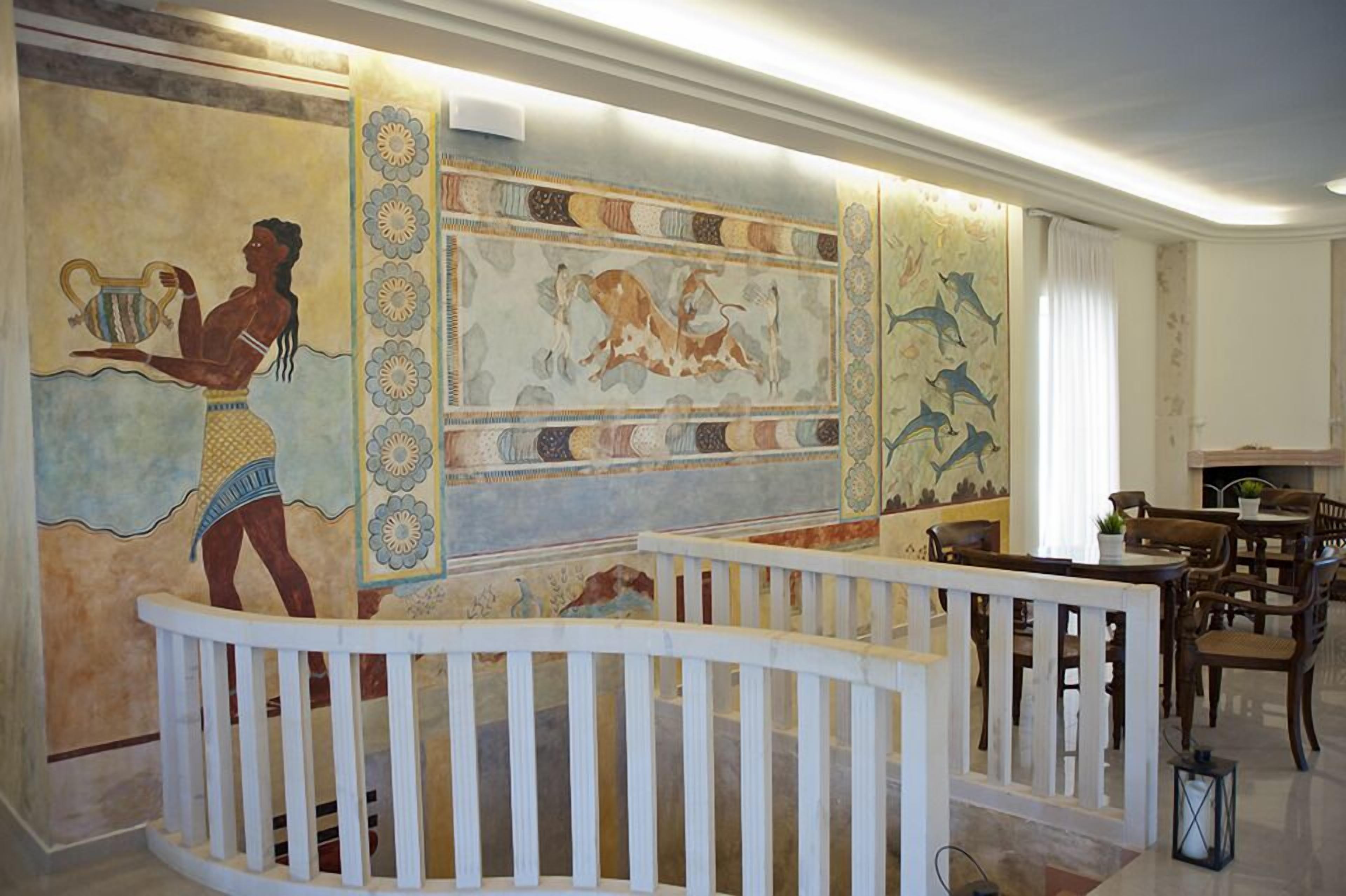 Een kamer met een muurschildering van oude Egyptische figuren, een witte balustrade en een eetgedeelte met houten meubilair.
