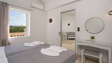 A hotel room with two beds, a desk, a mirror, and a view of the outdoors.