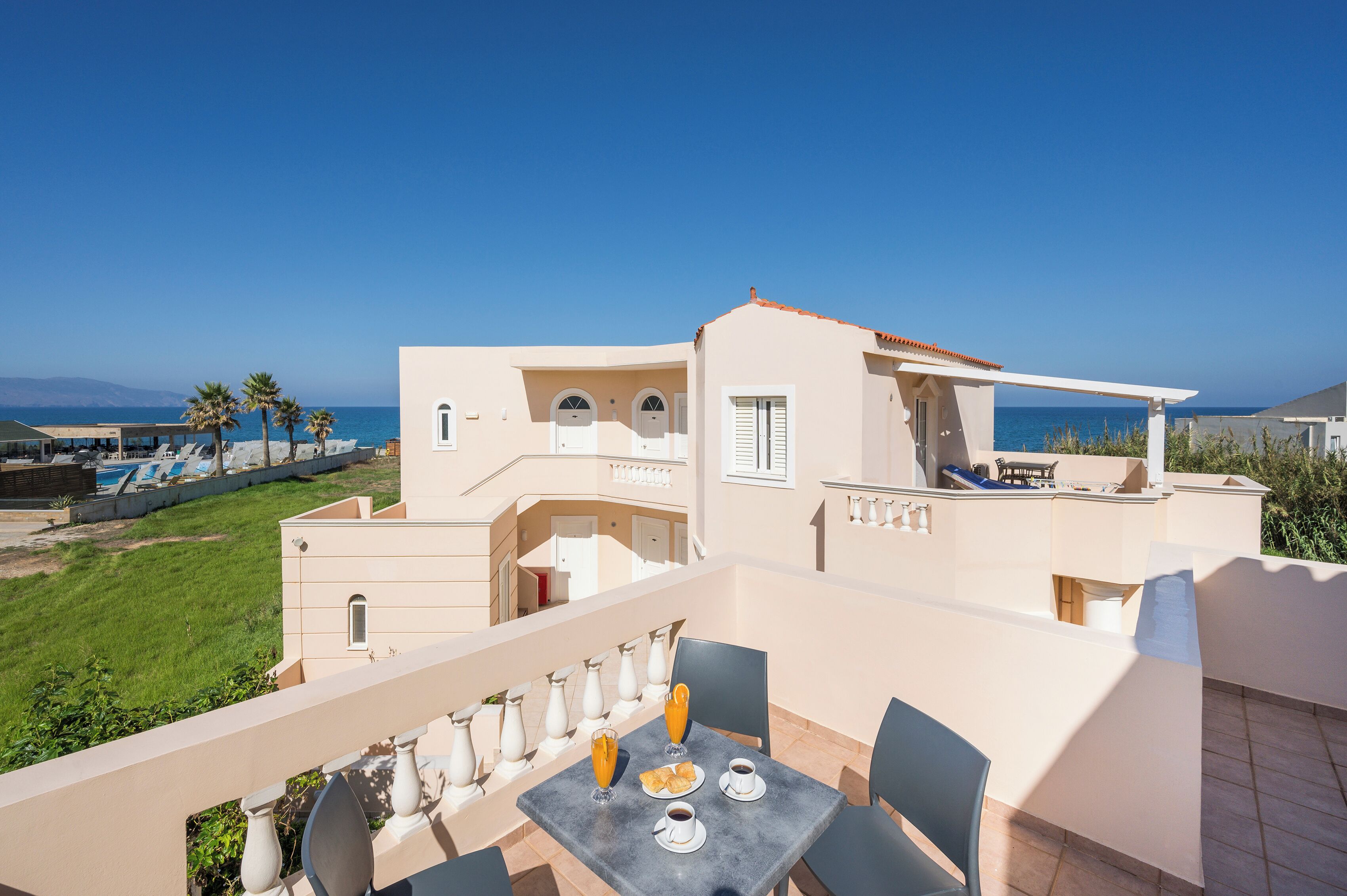 A balcony with a table set for breakfast, overlooking a pool and a clear blue sky.