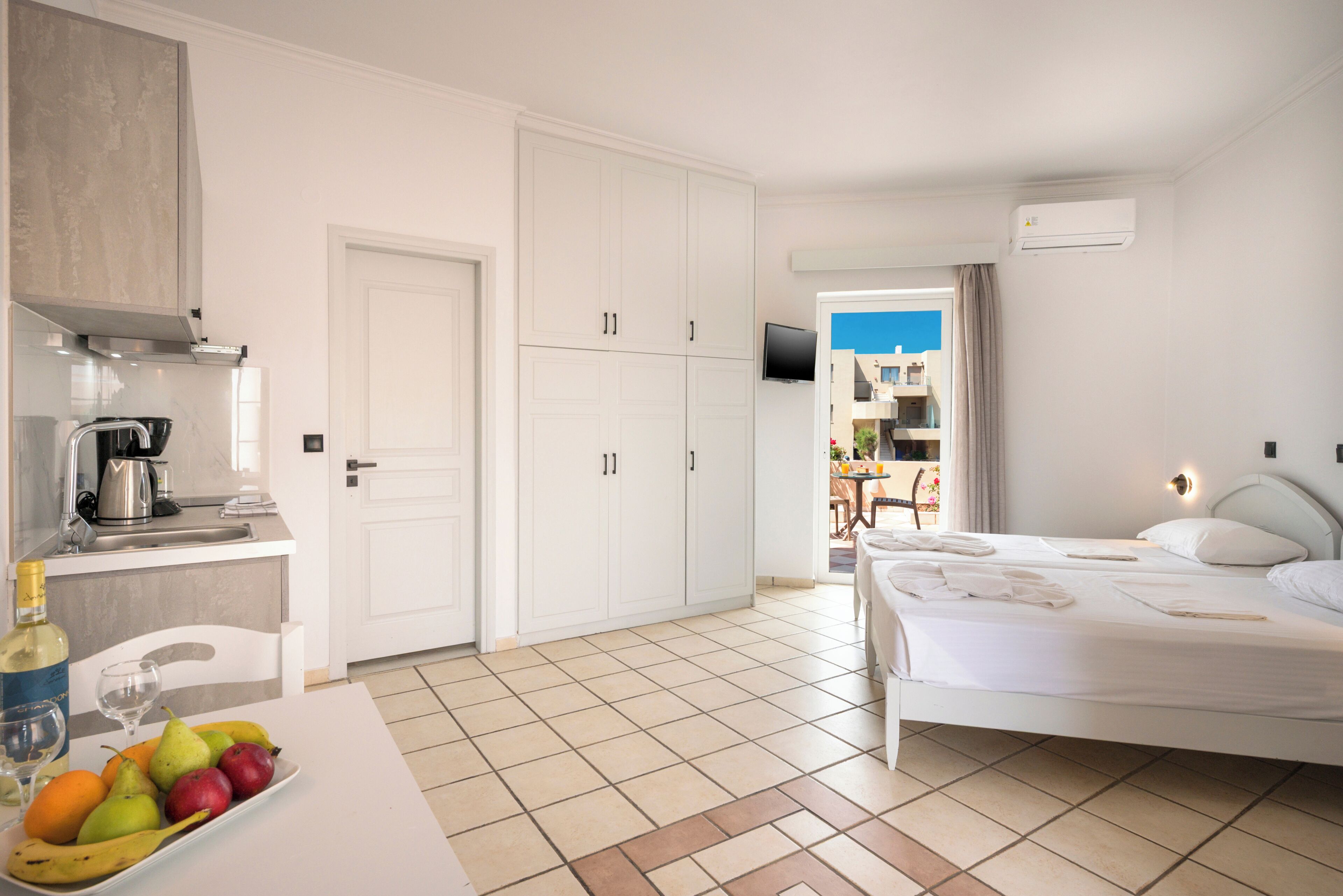 Habitación de hotel con cama, una mesa de comedor con fruta, zona de cocina y vistas al exterior.
