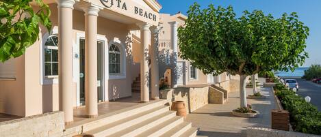 A building labeled "Caretta Beach" with a staircase leading to the entrance, a tree-lined pathway, and a view of the sea in the background.