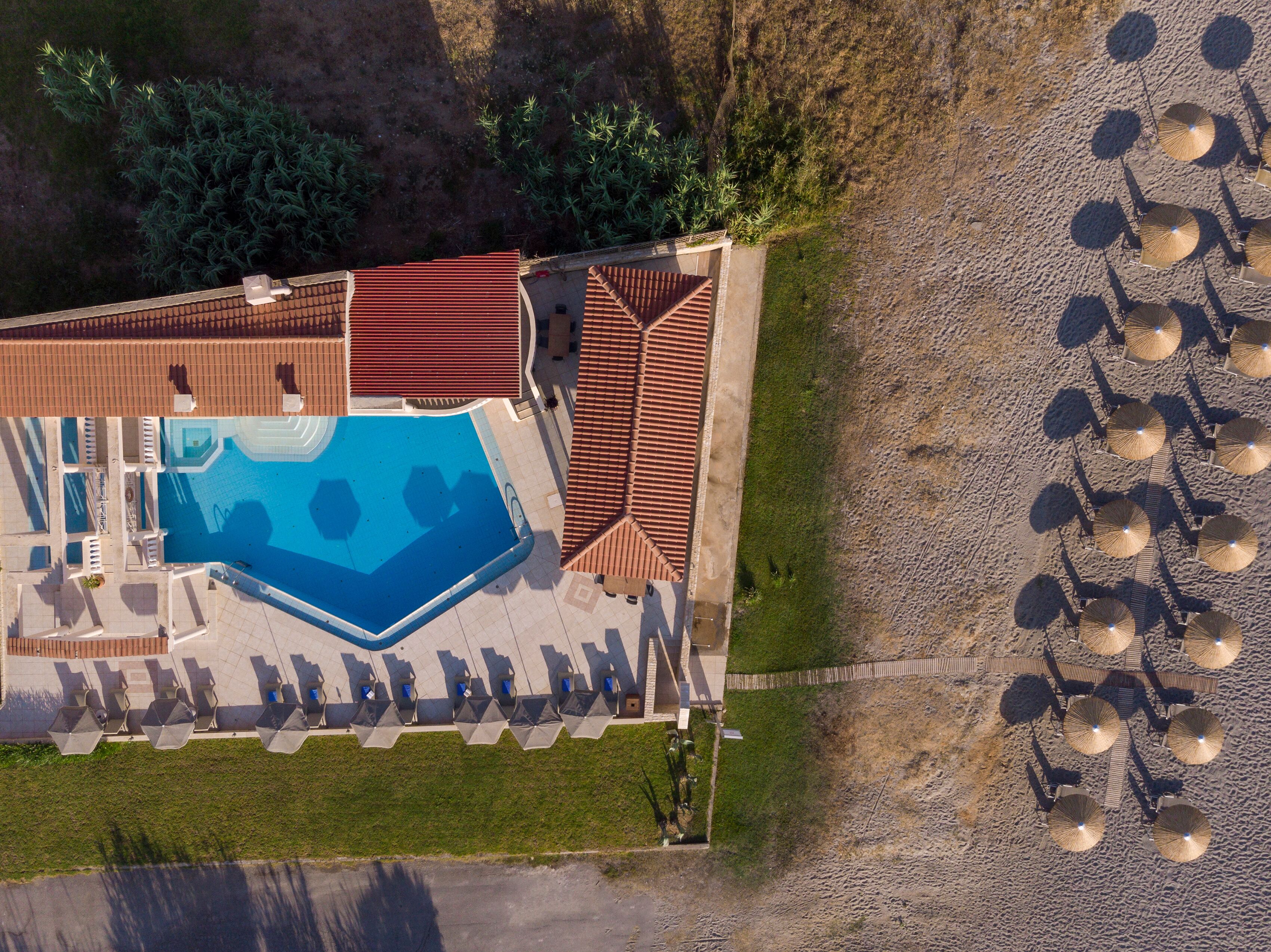 Vista aérea de un resort con piscina, tumbonas y sombrillas de playa.