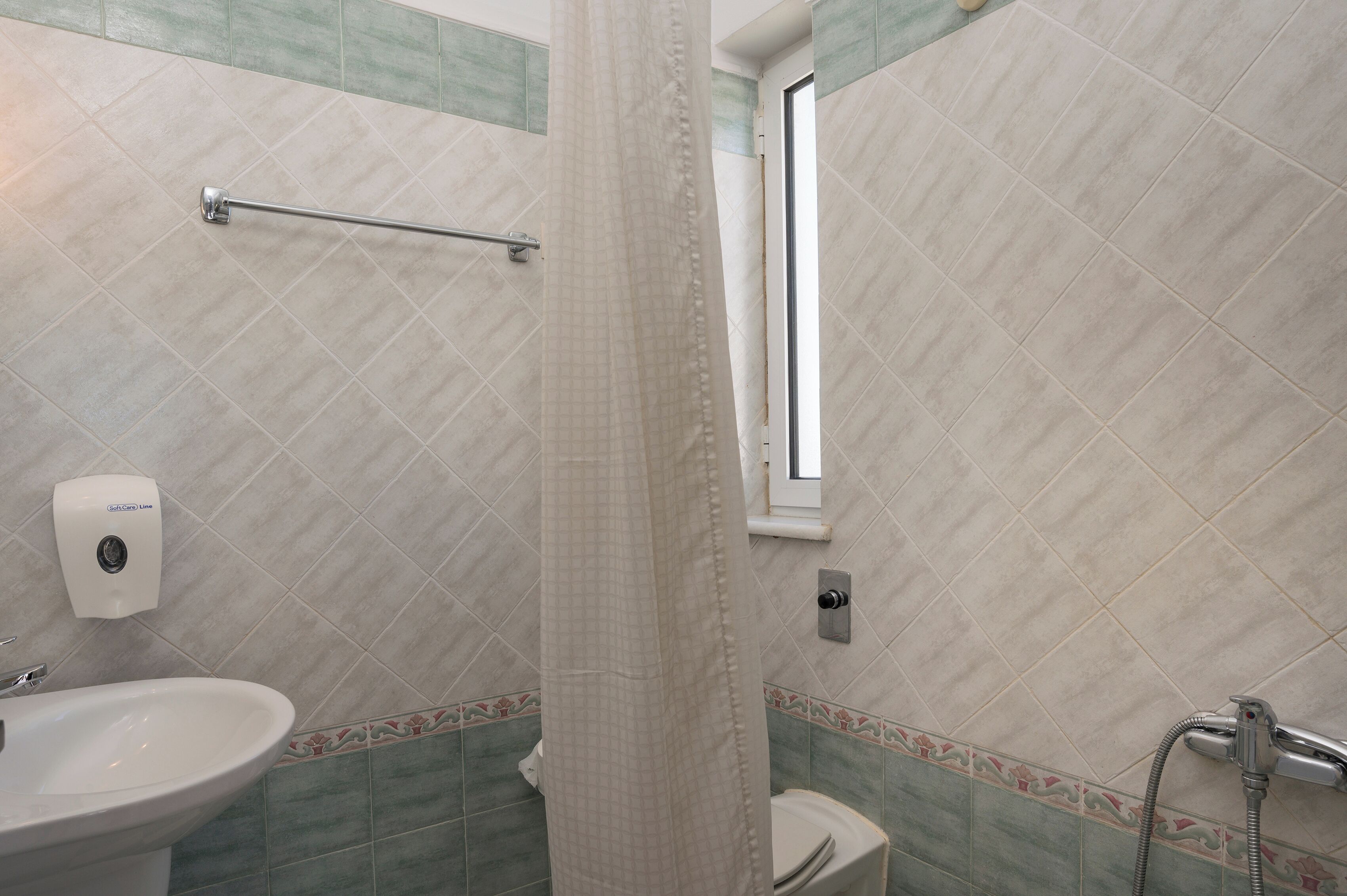 A bathroom with a shower curtain, a hand dryer, a toilet, and a sink.