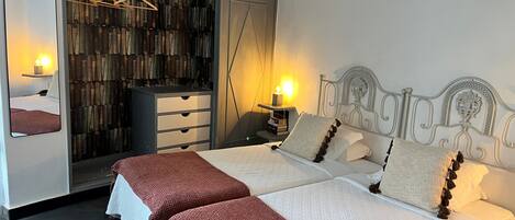 Una cama doble con cabecera, una mesita de noche con lámpara, un armario con espejo y un perchero.