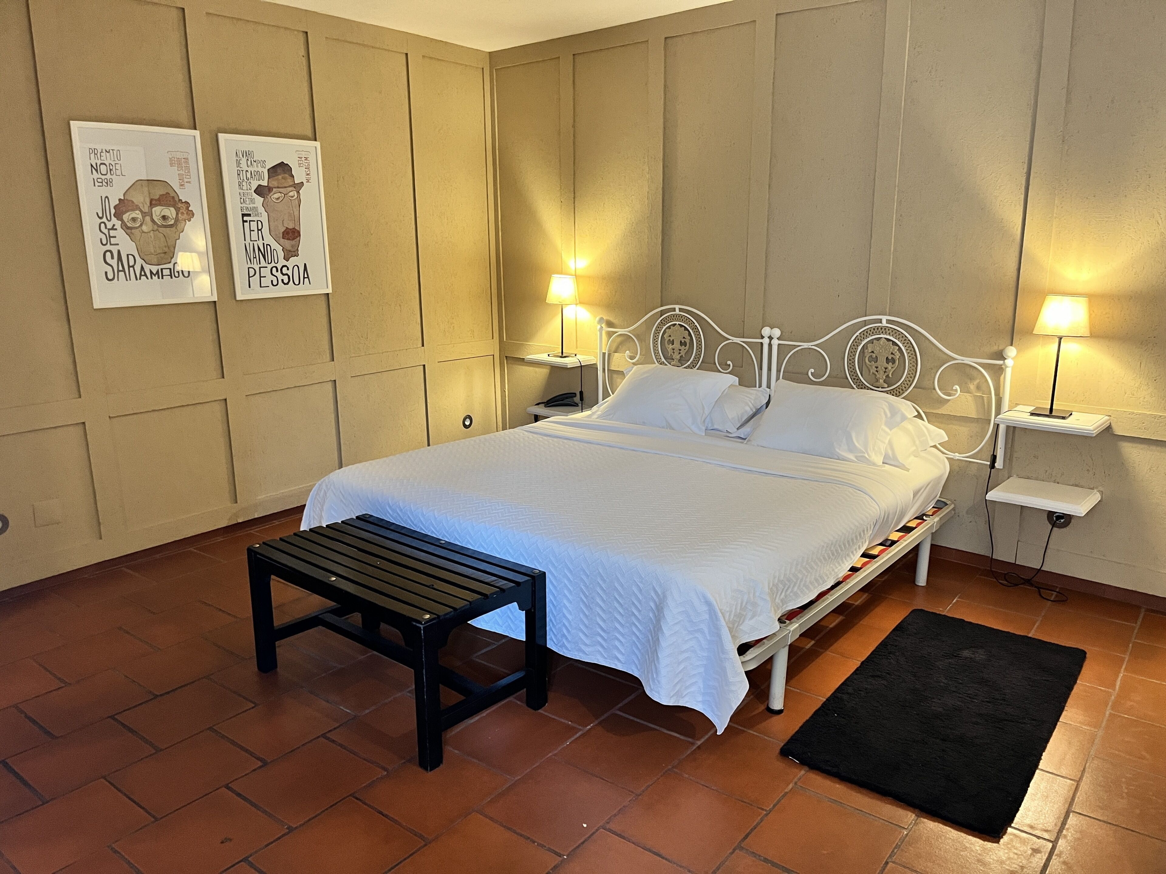 A neatly arranged bedroom with a bed, bedside tables, a bench, and two wall-mounted lamps.