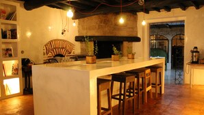 Una cocina con isla central, taburetes de bar, chimenea de piedra y lámparas colgantes.