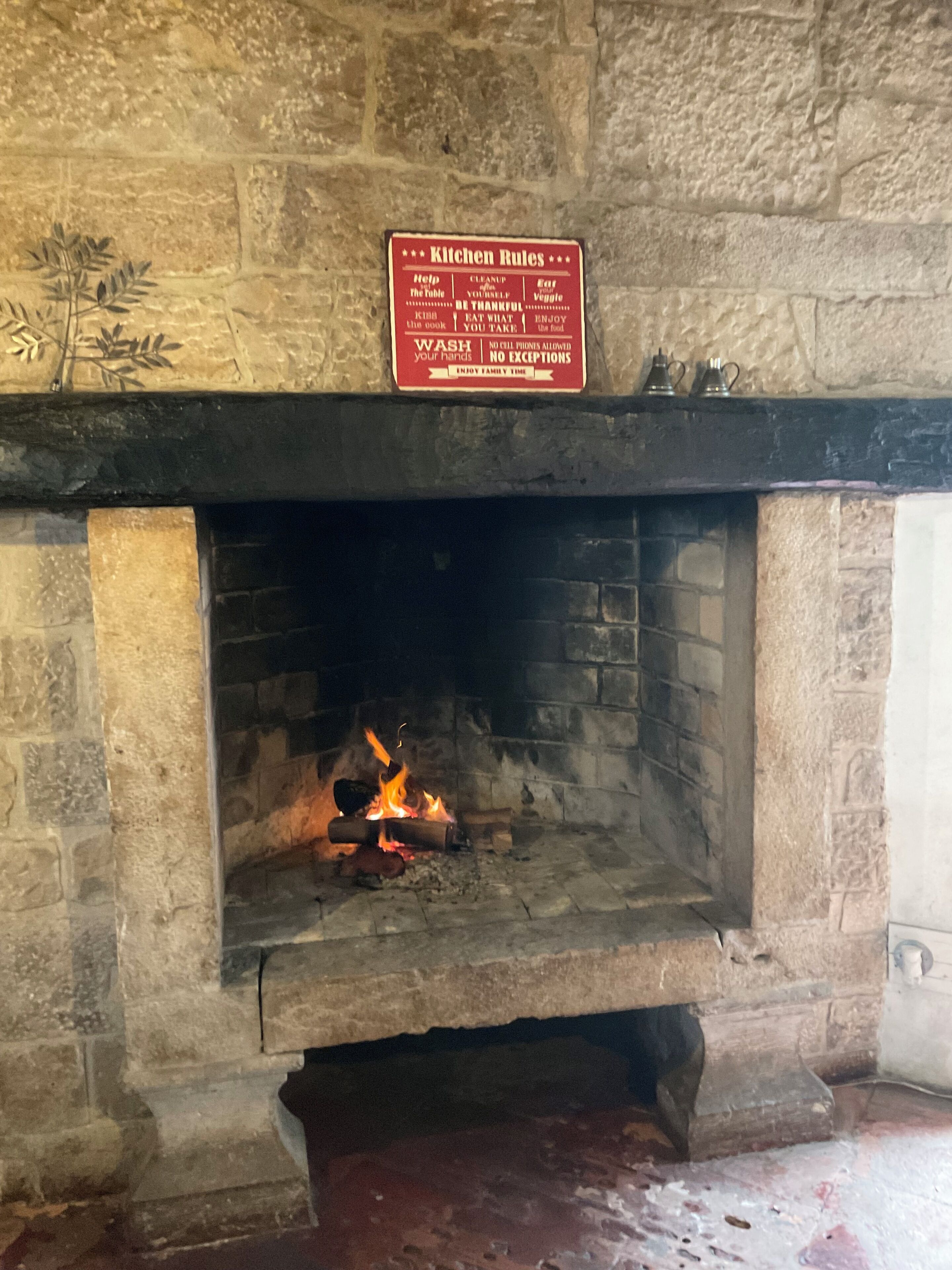 A stone fireplace with a sign above it listing kitchen rules.