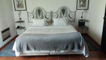 A neatly made bed with a grey and white duvet, two white pillows, and a decorative metal headboard. There are two bedside tables with lamps, and two framed pictures on the walls.