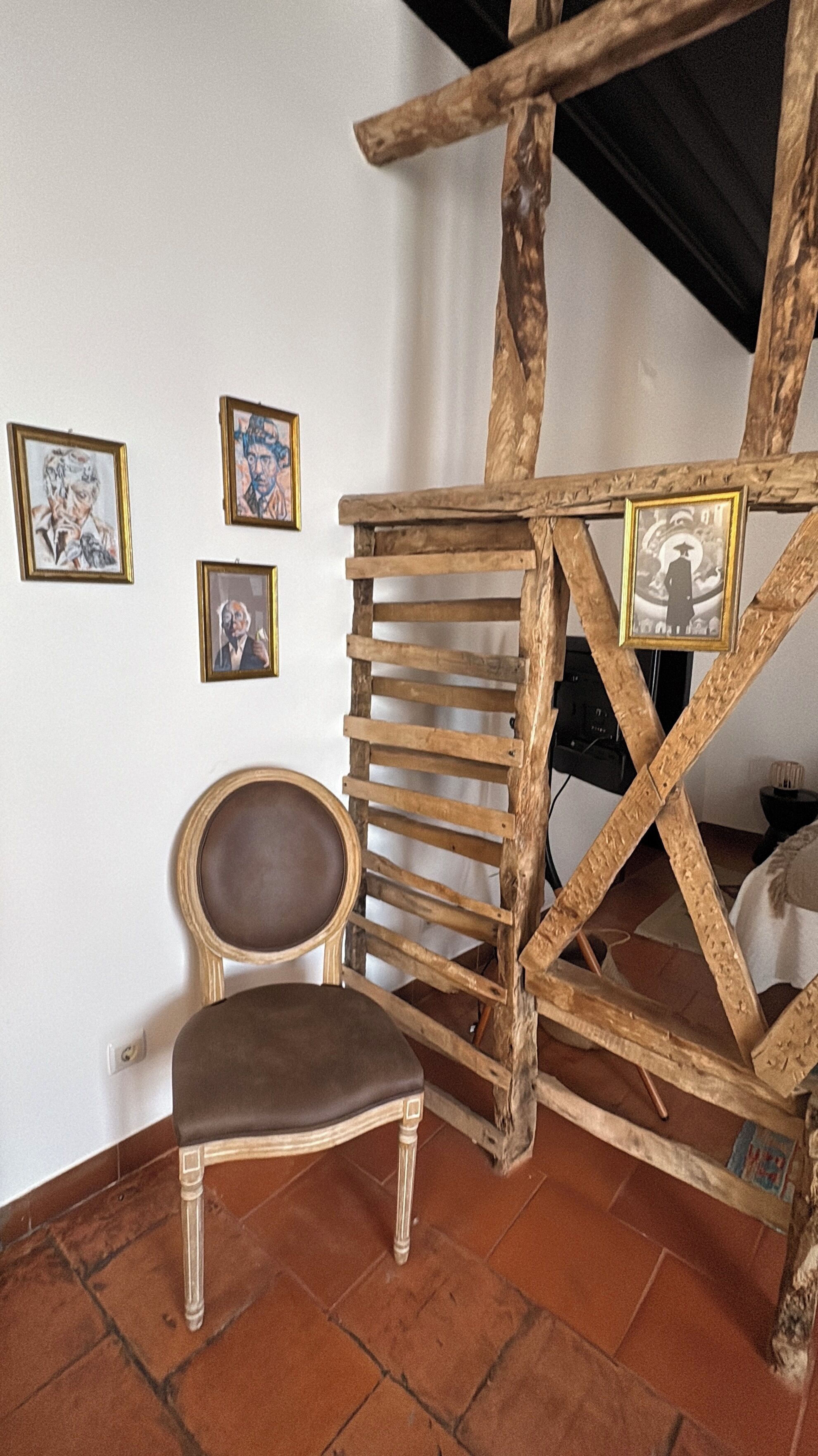 Um quarto rústico com uma escada de madeira, uma cadeira e quadros na parede.