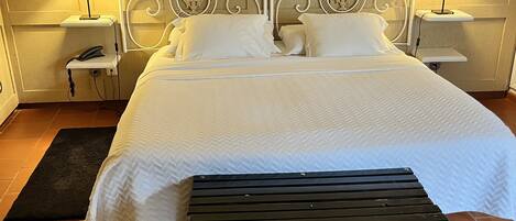 A neatly made bed with white linens, a black bench, and two bedside lamps on matching nightstands.