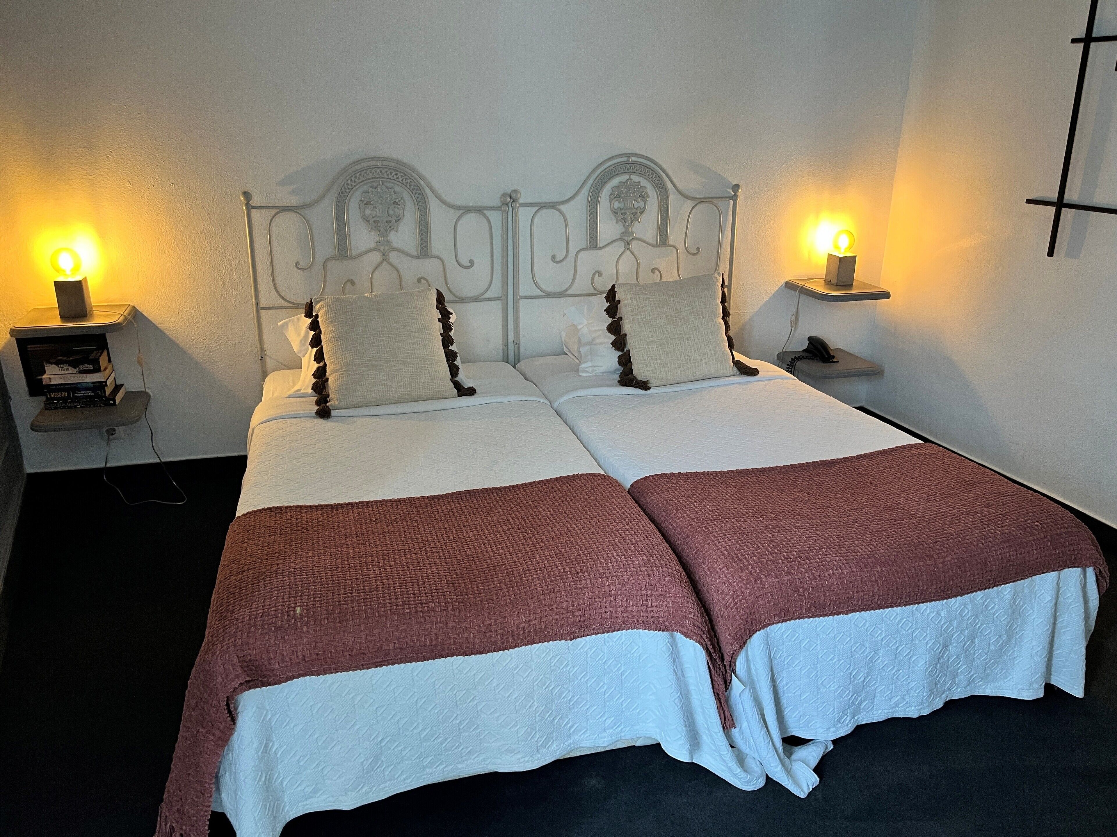 A double bed with a white and brown bedspread, two bedside tables with lamps, and a wall-mounted light fixture.