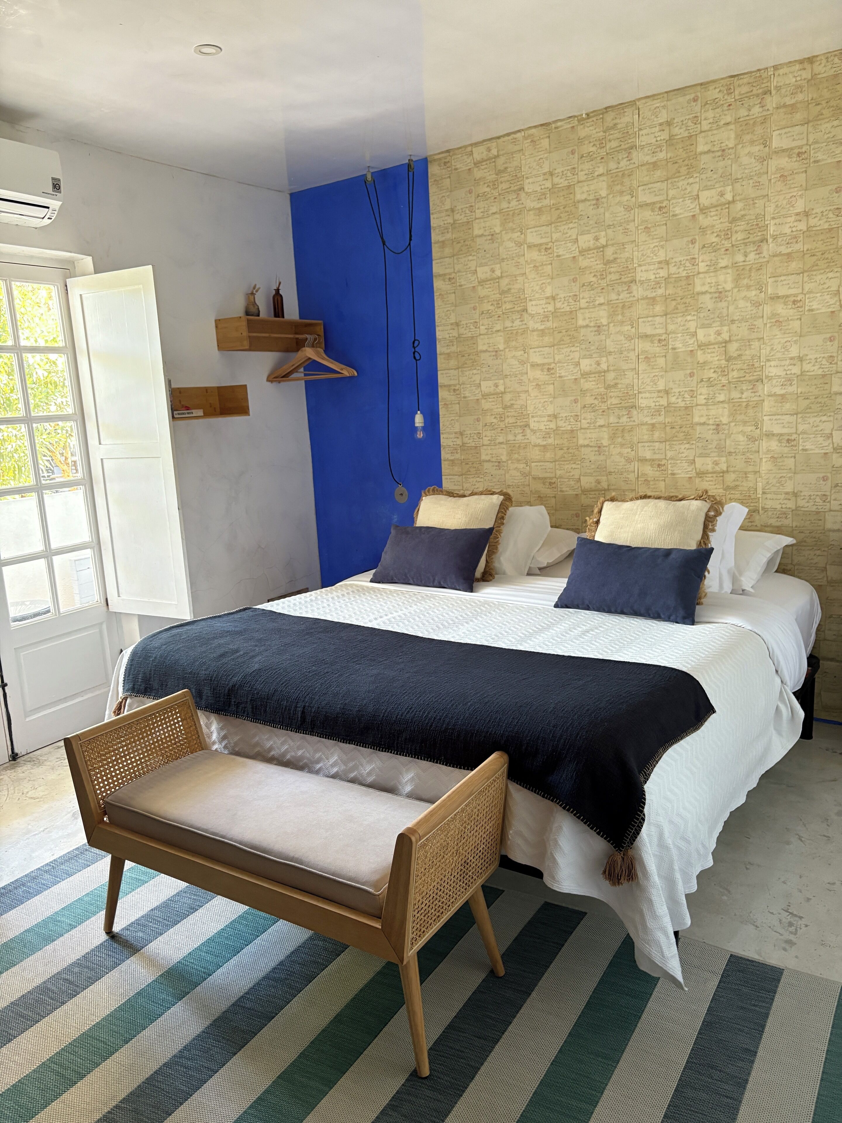 A bedroom with a large bed, a bedside table, a chair, a wall with a blue accent, and a window.